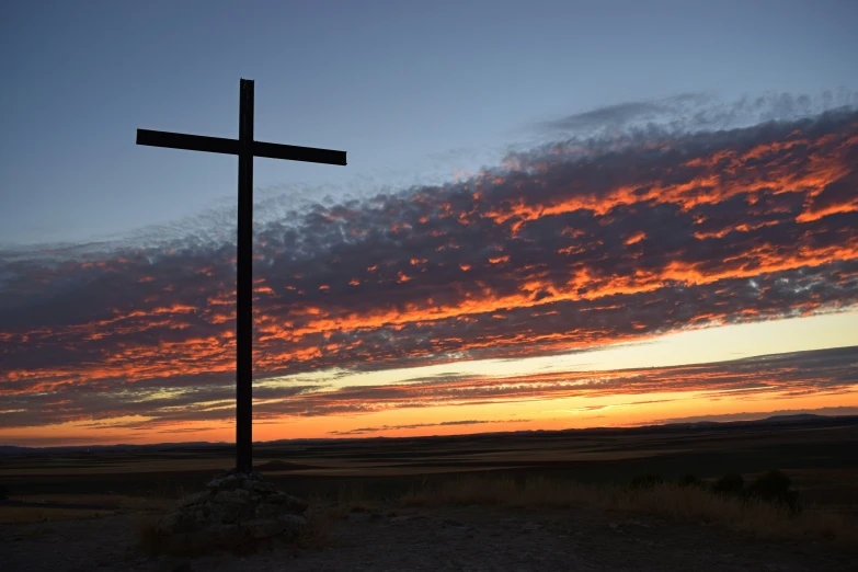 a cross sitting in the middle of a field with clouds