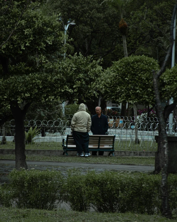 two people sit on a park bench, the man is talking to the woman