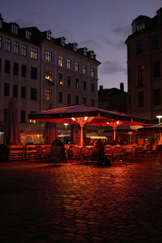 a row of buildings at night with lit up tables and chairs