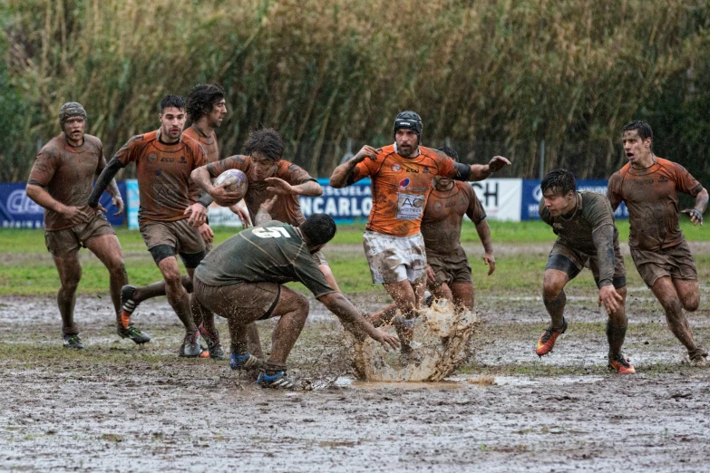 many men play in a mud - covered field while one kicks it