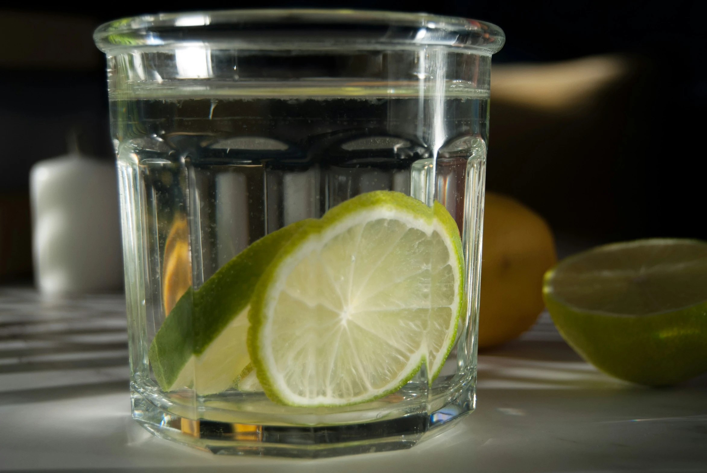 a glass of water with some limes near it