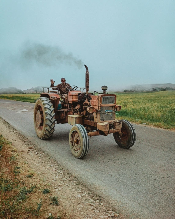 a tractor driving down a dirt road with some steam pouring out of it