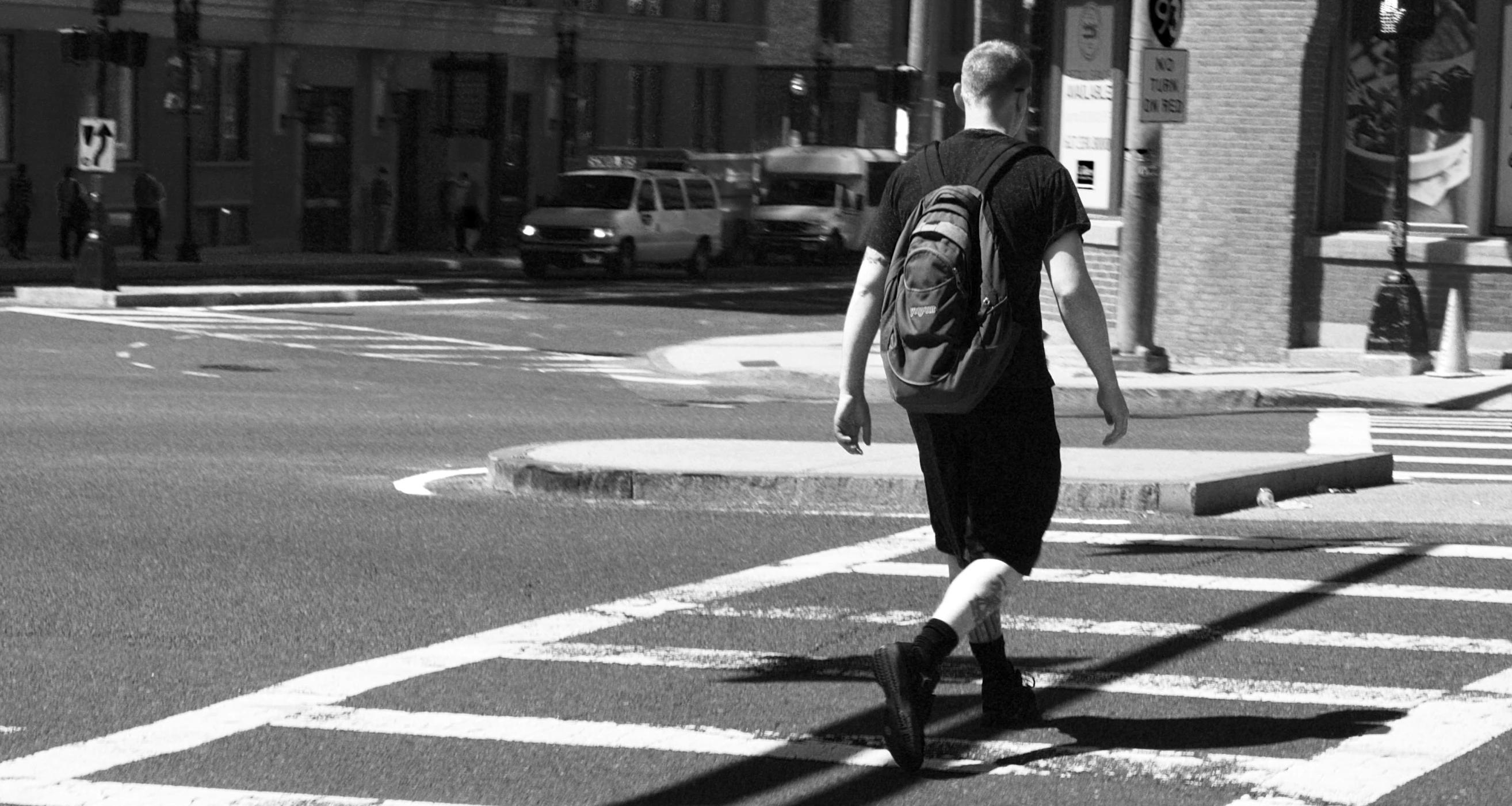 man walking across a cross walk with a backpack