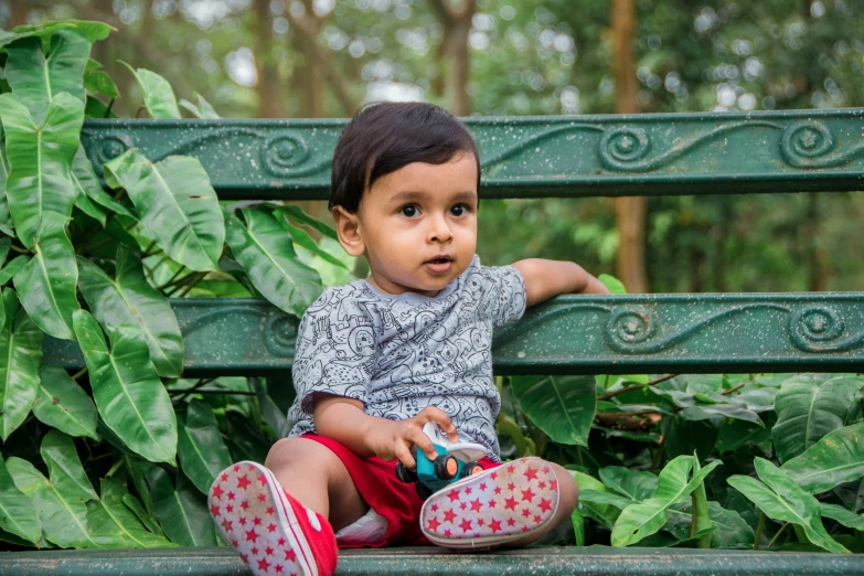 a little boy sitting on a bench in a park