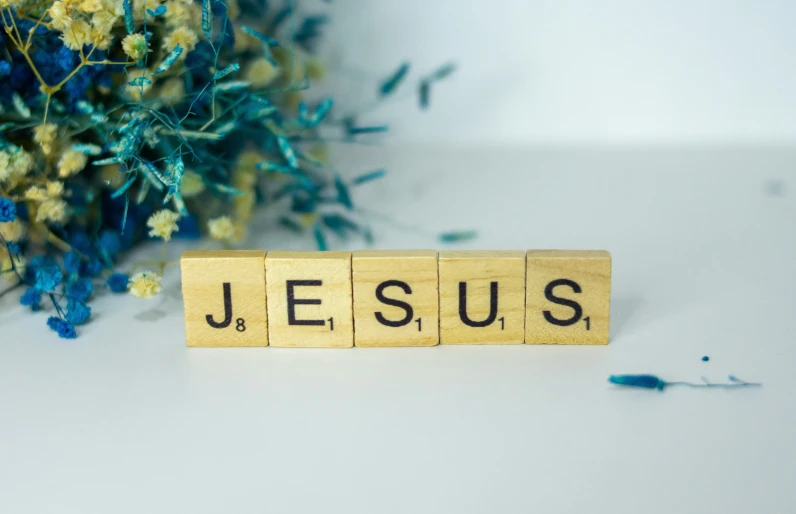 wooden blocks spelling jesus on a table with flowers