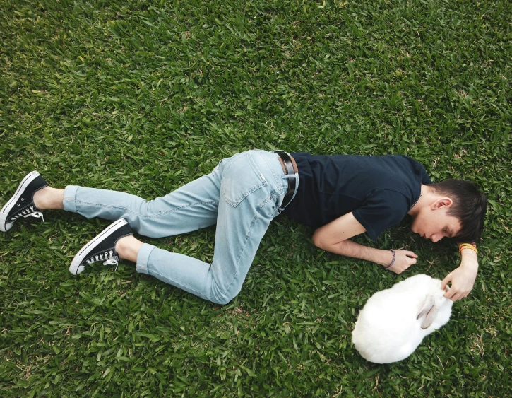 a man lays on the grass with his white bunny