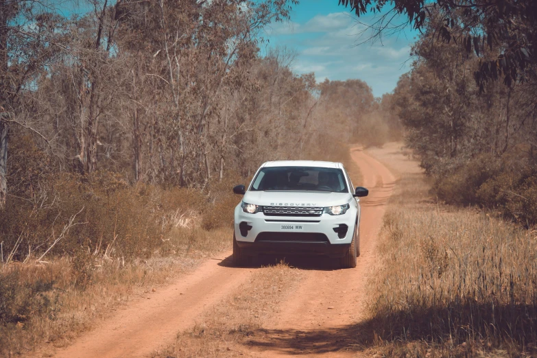 the white car is traveling along the dirt road