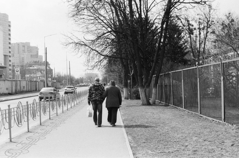 two people walking down a sidewalk by a fence