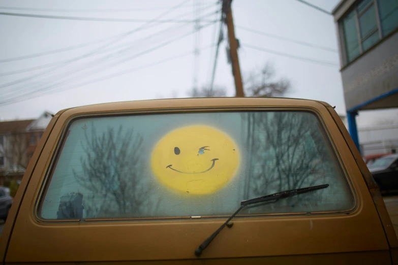 an angry yellow smiley face drawn on the window of a small truck