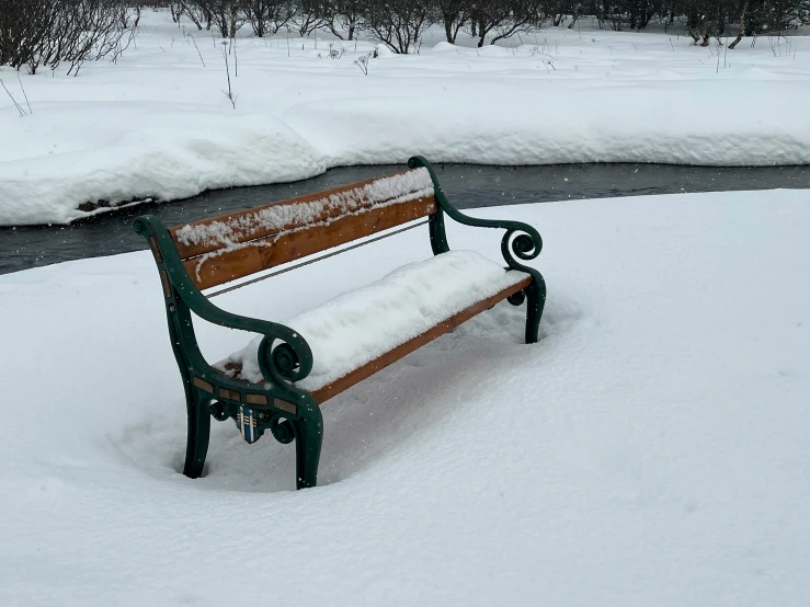 a bench sitting in the snow by a small stream