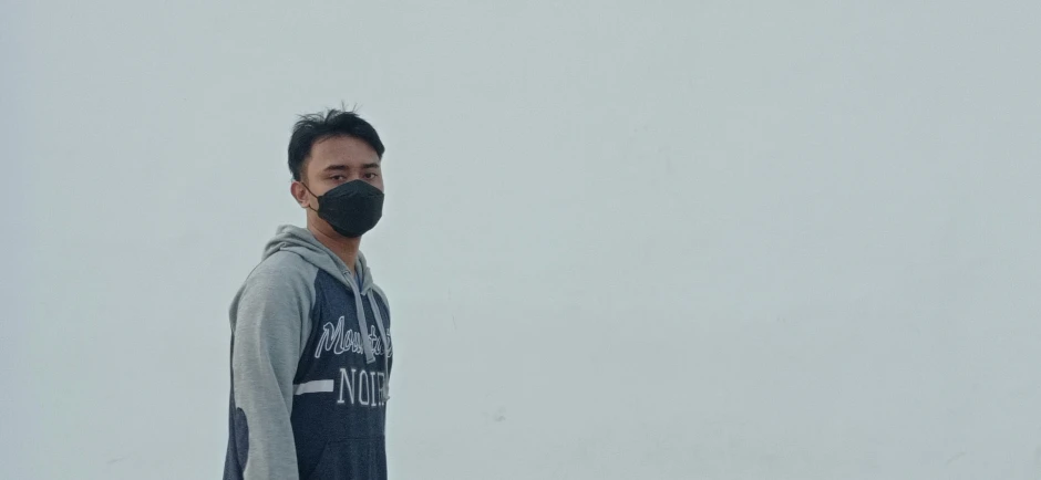 a man wearing a black face mask stands outdoors