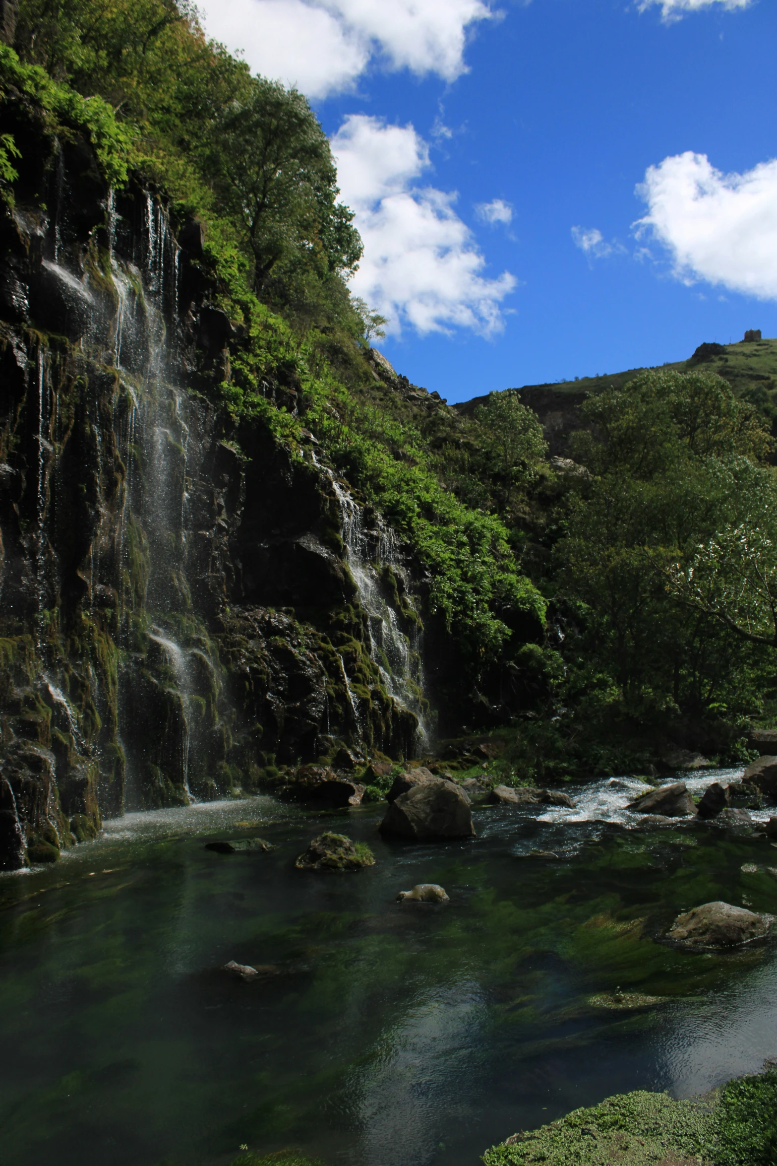 a stream flows by tall waterfalls on the side of a hill