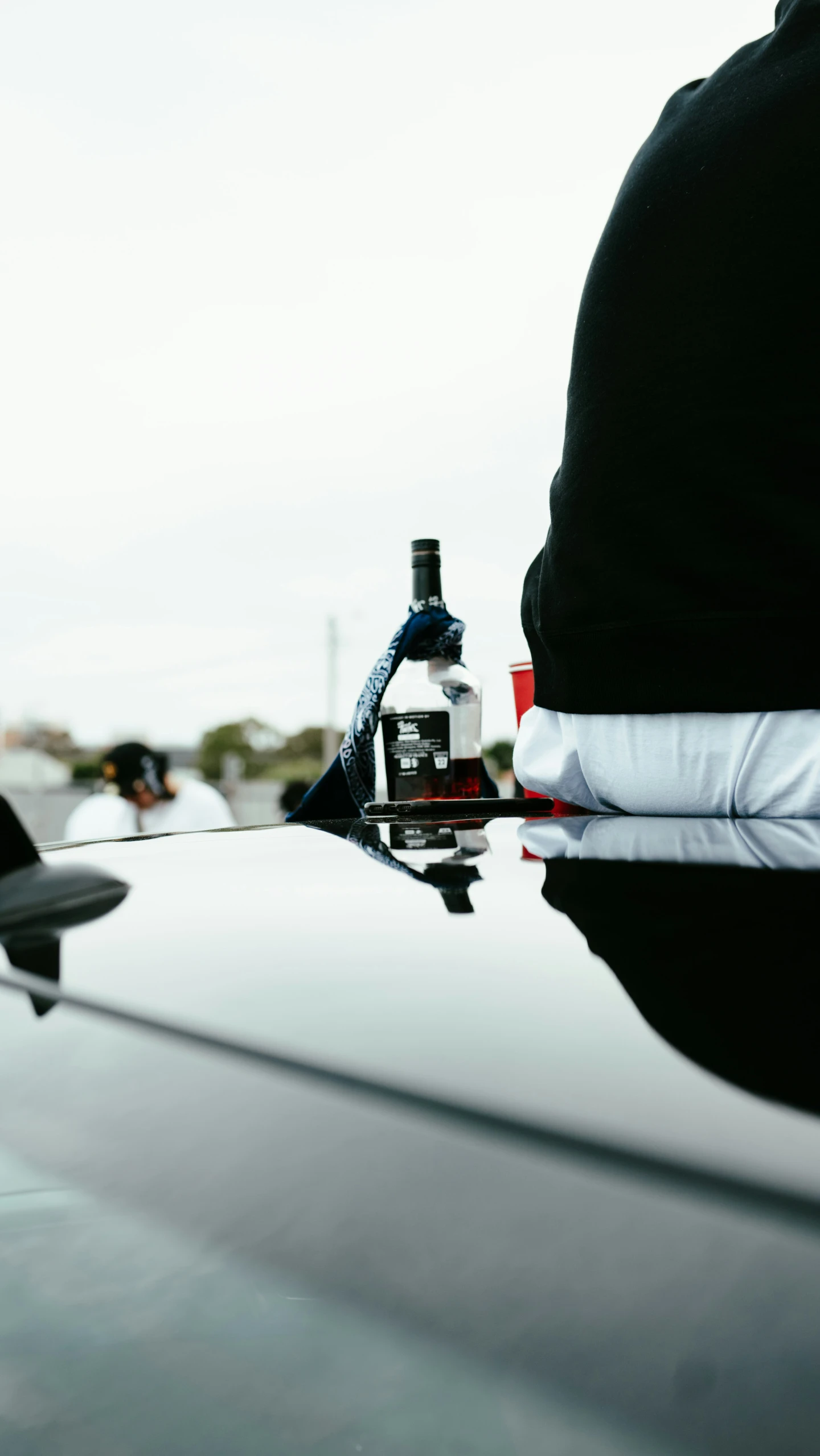 a person's feet in the hood of a sports car with bottles of alcohol on top