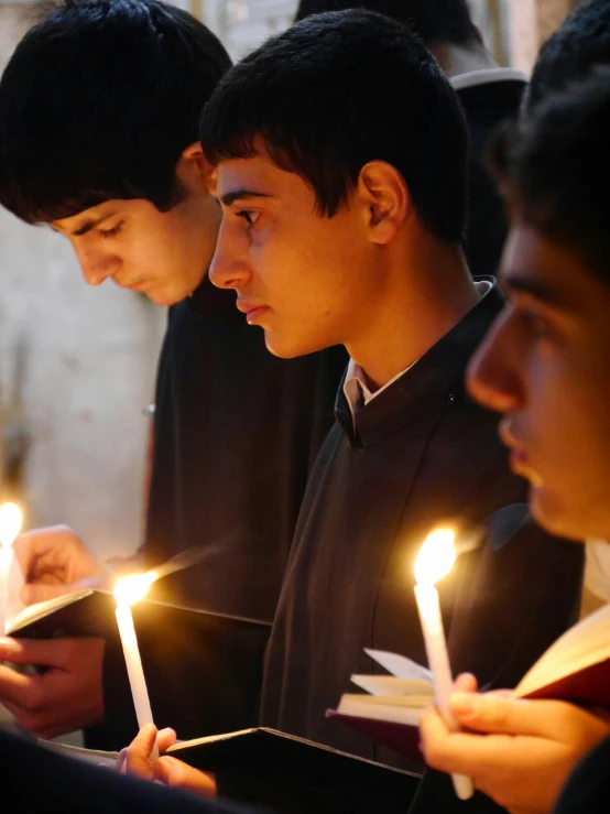 people hold lit candles as they are reading in the chapel