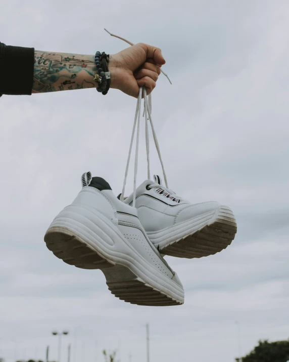 two white shoes hanging on strings with a hand