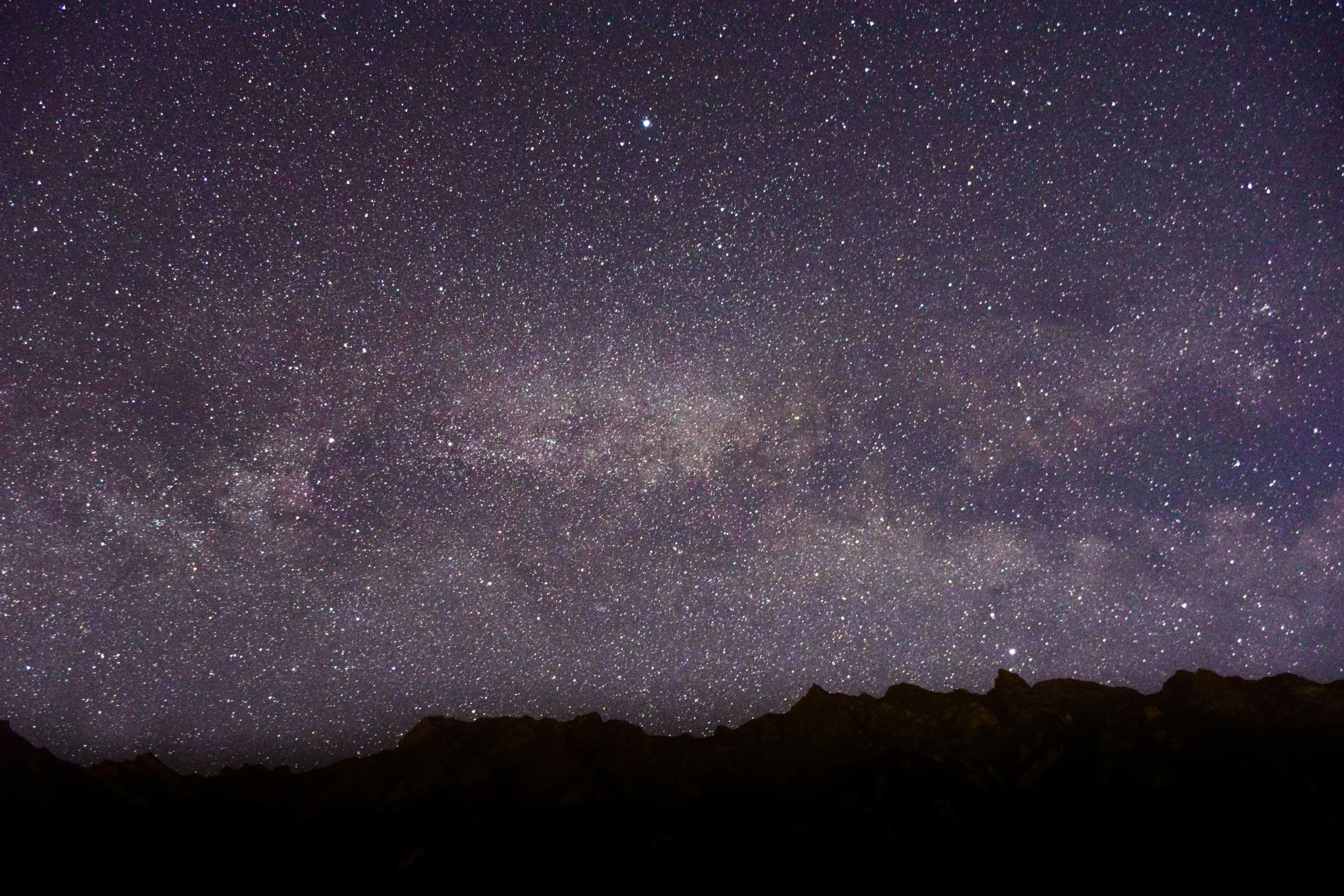 a dark sky and stars above some mountains