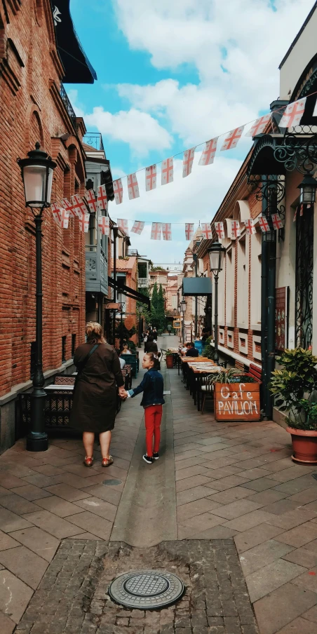 two people walking down an alleyway next to tables