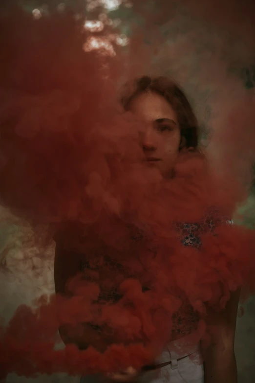 a person holds a small cloud of red substance while staring