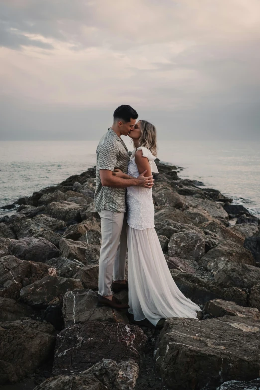 a man and a woman standing on rocks next to the ocean kissing
