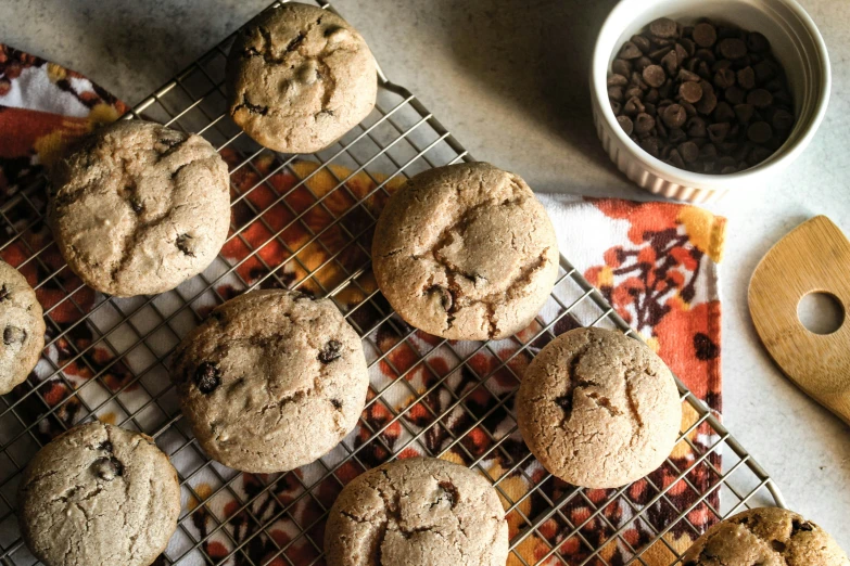 twelve cookies sit on a wire rack beside a measuring cup