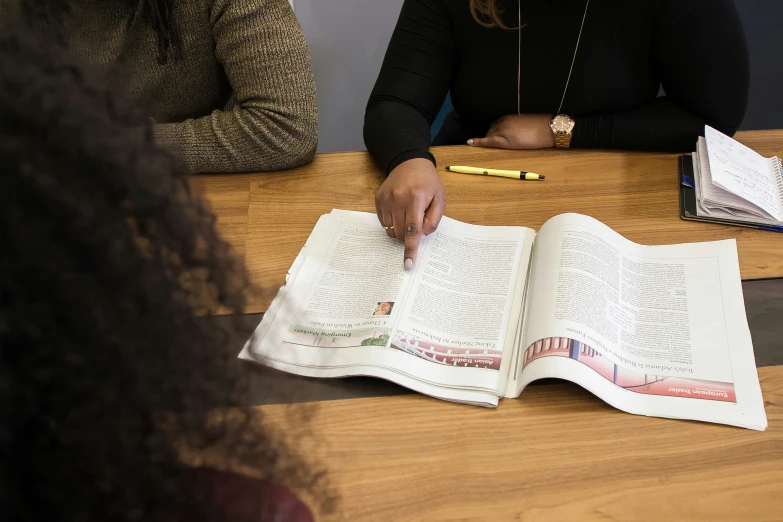 two women are sitting at a table and reading a book