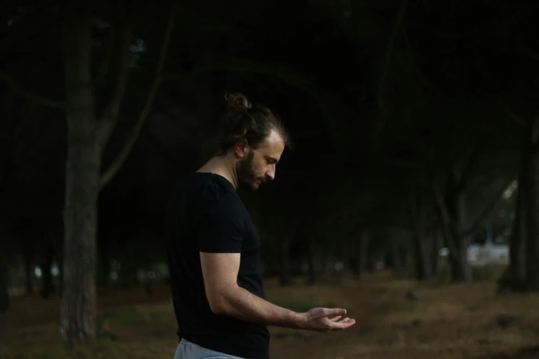 a young man standing by some trees looking away