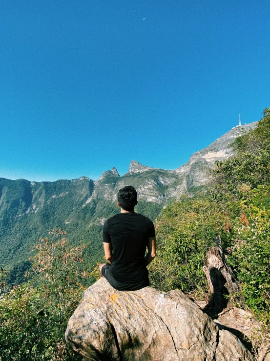 a person is sitting on the rock looking at mountains