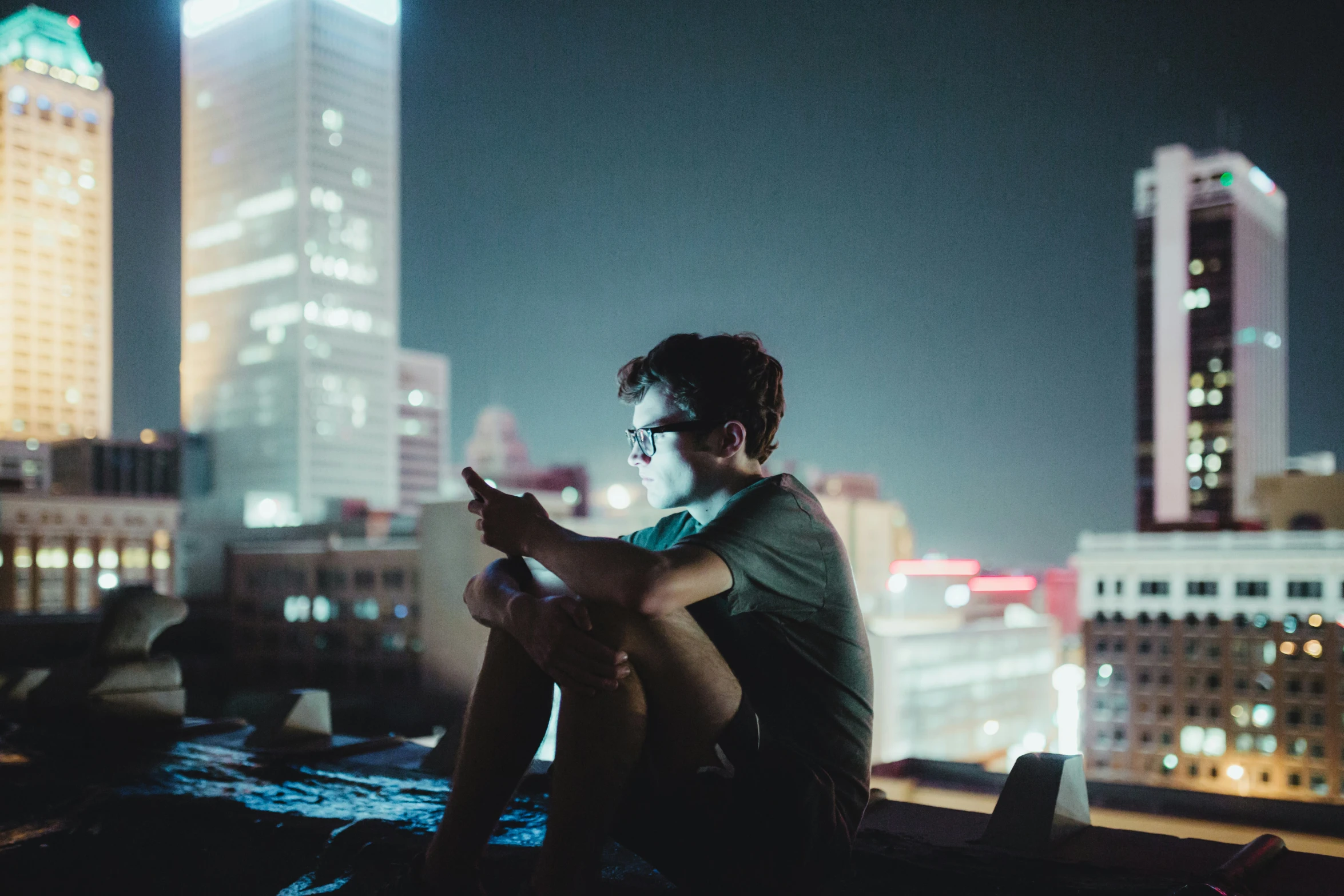 man using cell phone sitting on rooftop at night