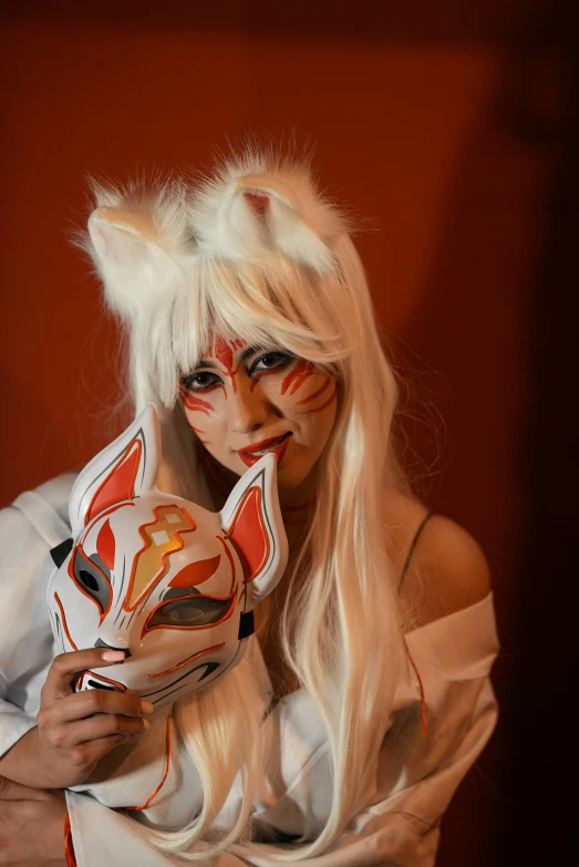 a woman with painted makeup is holding a cat mask