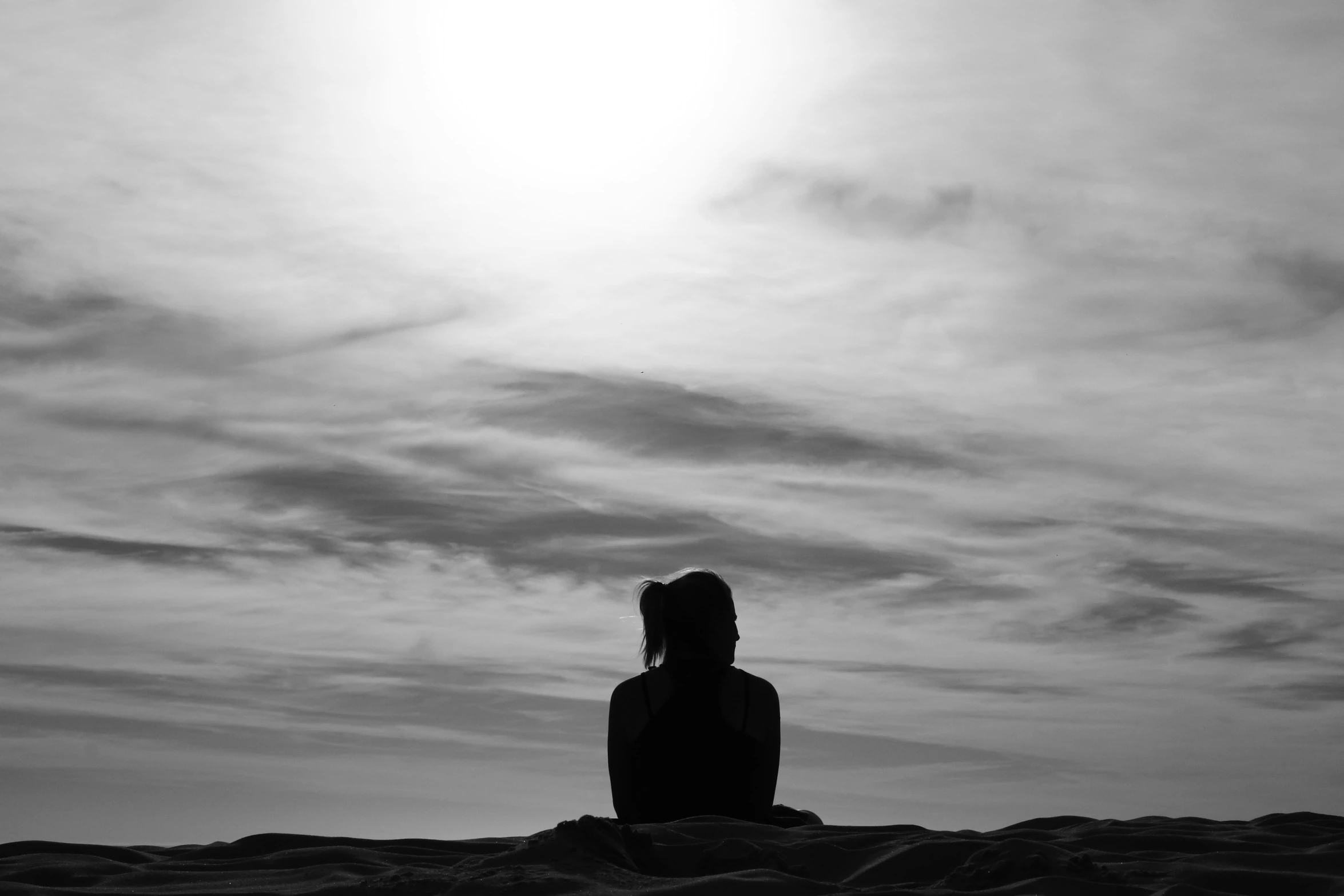 the silhouette of a person seated on the sand