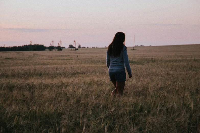 a girl is walking in a field at dusk