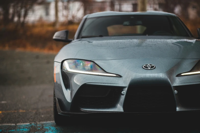 the front end of a grey sports car on a wet road