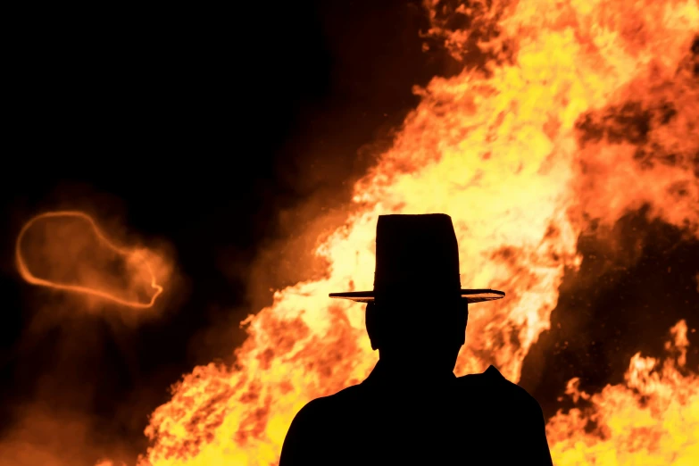 man in black coat and hat with a blazing background