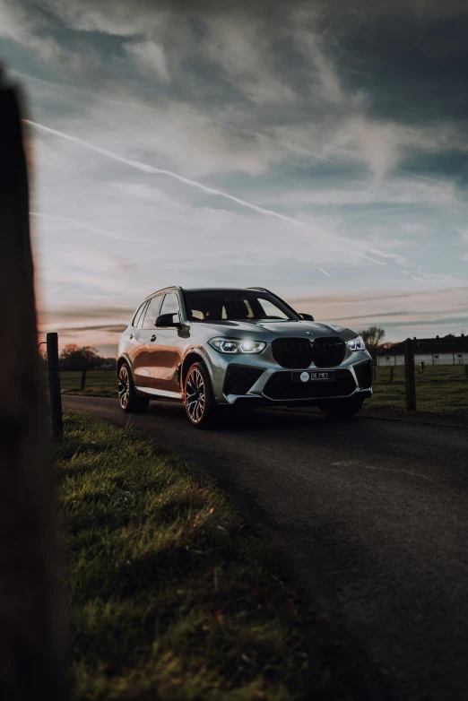 the bmw x5 with orange rims is driving on a country road