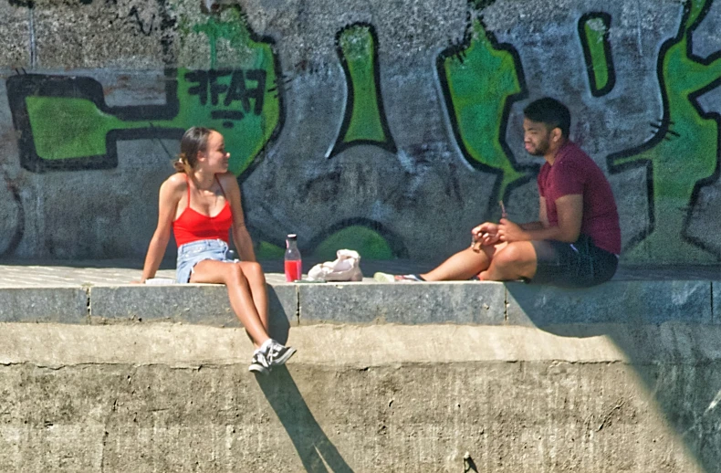 two people sitting on concrete by some graffiti