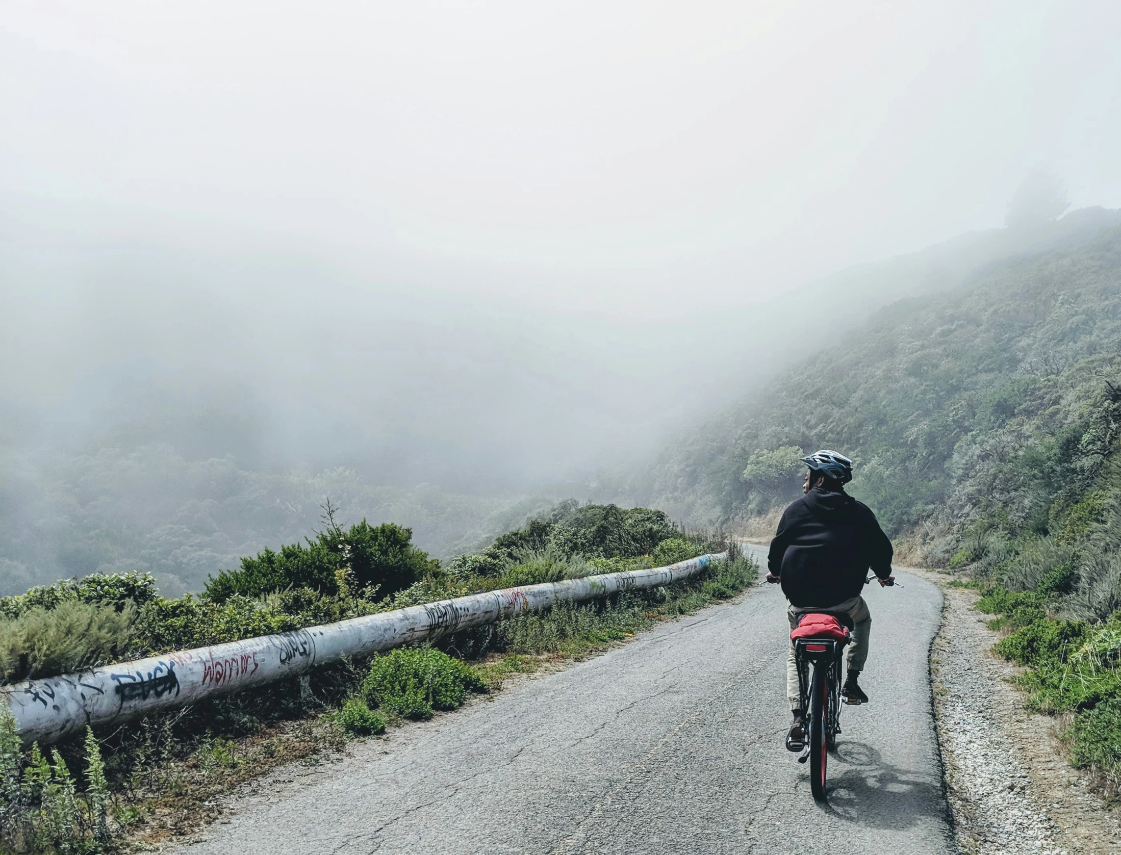 a bicyclist rides down a road through foggy hills