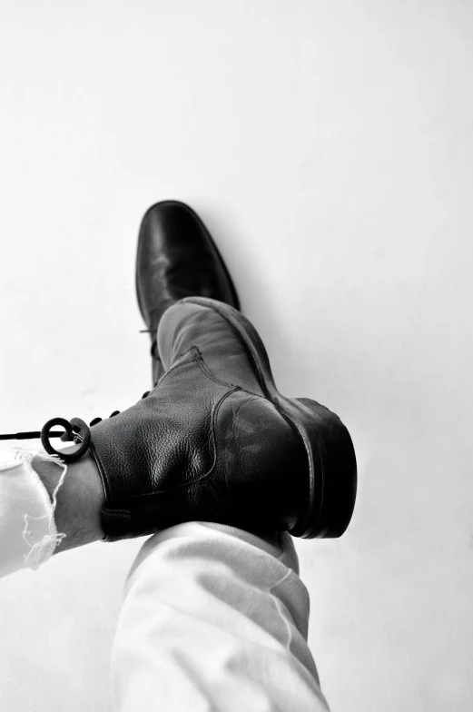 the legs of a person in white pants and a pair of black boots, holding a pair of scissors