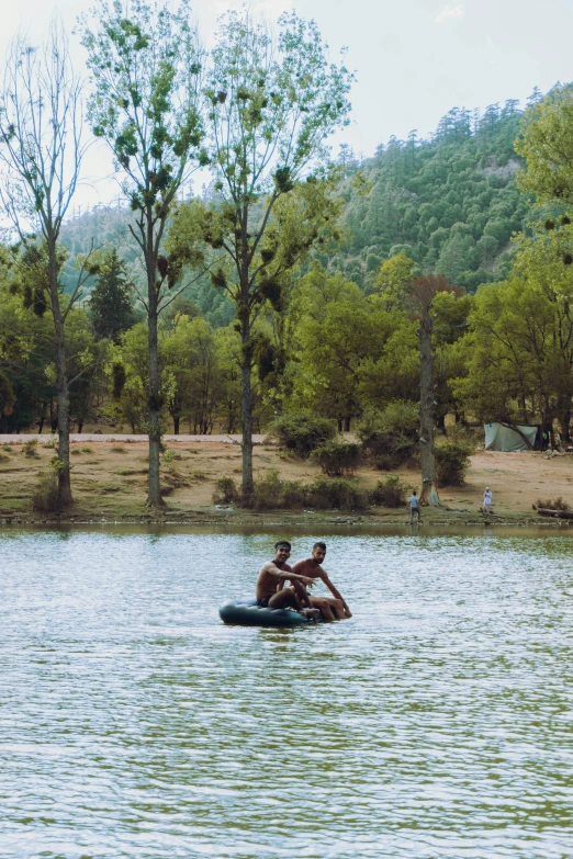 two people ride in the middle of a lake while surrounded by trees