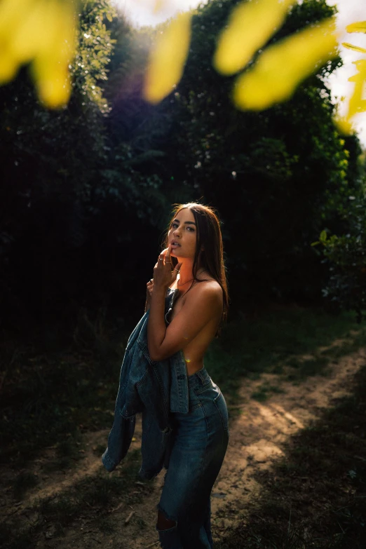 woman standing on dirt trail in wooded area smoking cigarette