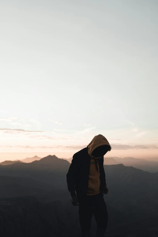 man with hood over his head standing on the edge of a cliff
