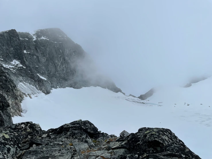 a mountain with snow near the summit with low clouds