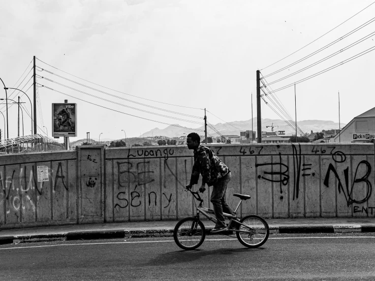 a man riding a bike past a fence with graffiti