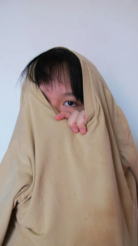 an asian woman peeks through a blanket to check on the camera