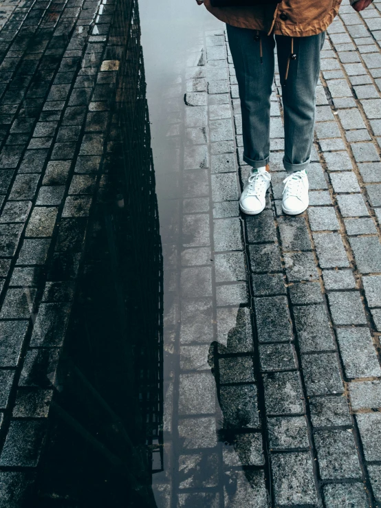 the person is standing on cobblestone beside the water