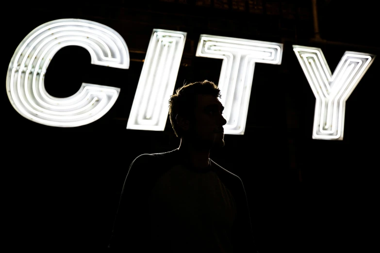 man standing in front of a lit sign with the city lights in the background