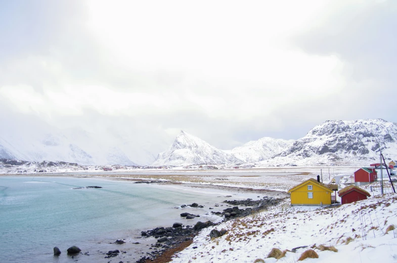 two red houses by the water on the side of the snow covered mountain