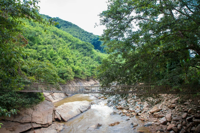 a bridge crossing a stream in front of a green mountain