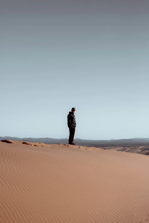 man in a hooded jacket standing on a sand dune