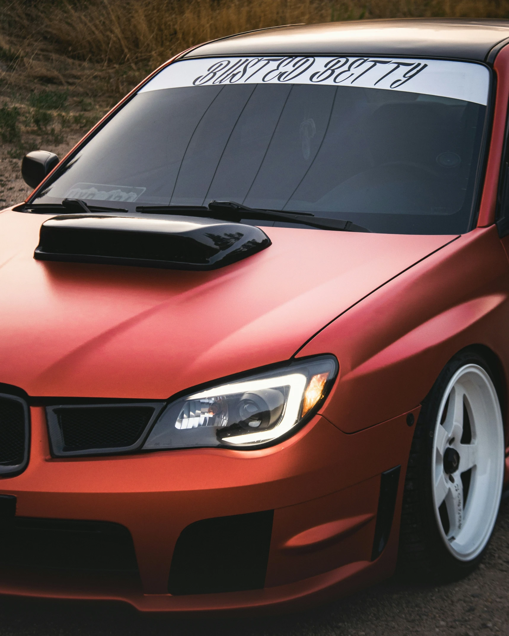 an orange car is parked on a dirt surface