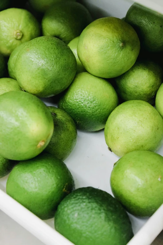 there is a small bowl with limes and a lemon in it